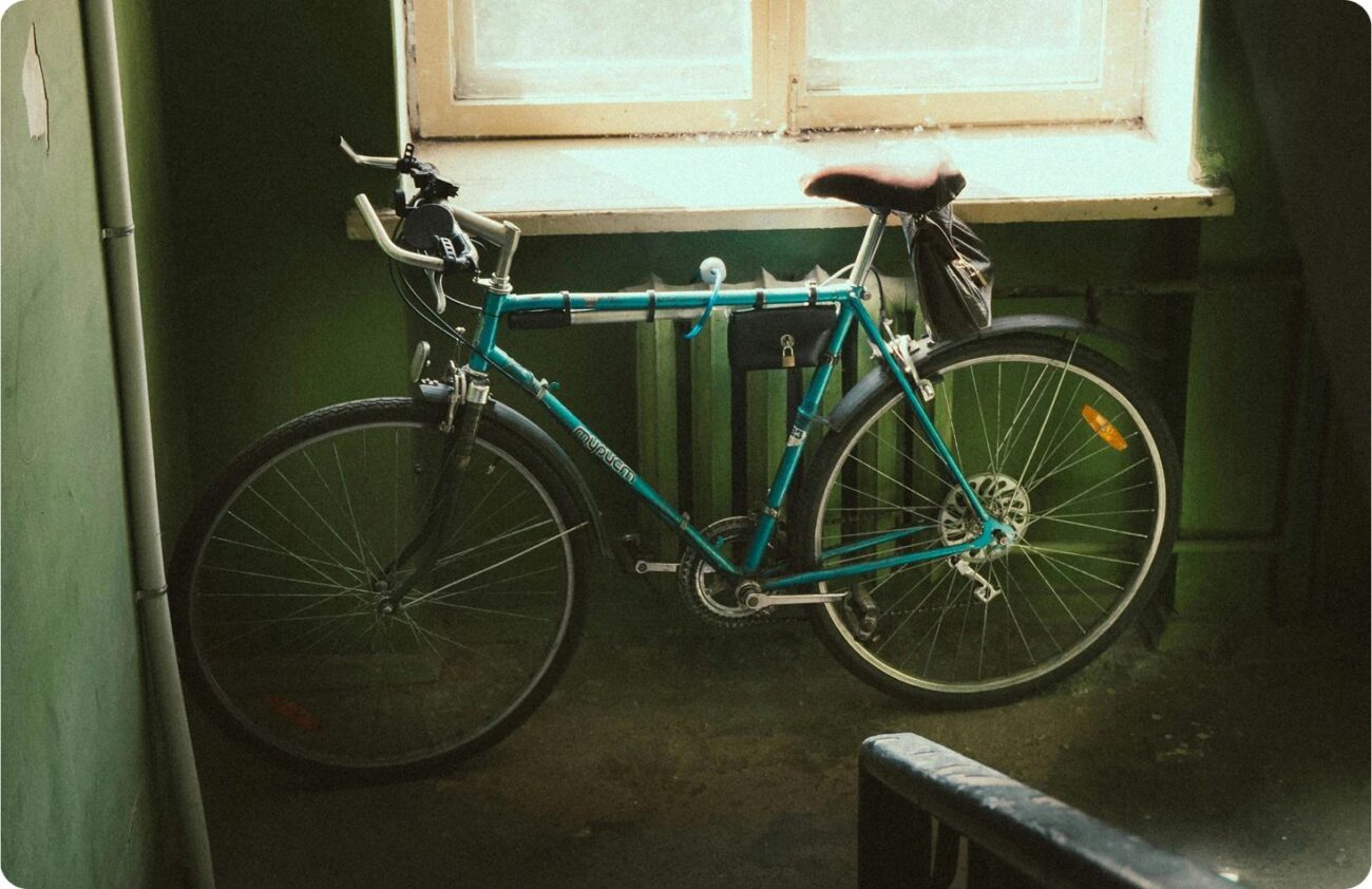 Un vélo de route ancien posé contre un mur, à la lumière d’une fenêtre